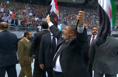 الرئيس مرسي يحيي الحضور رافعًا علمي مصر وسوريا بإستاد القاهرة